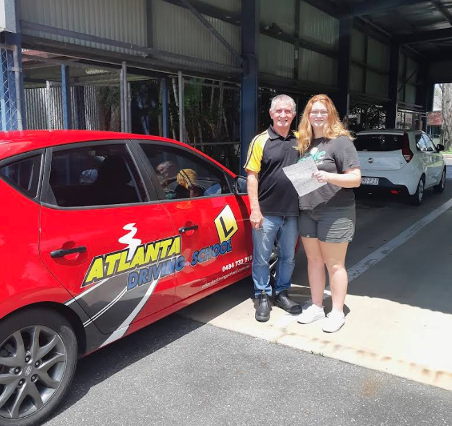 Atlanta Driving School instructor with a smiling student holding her Queensland driver licence receipt beside the branded training car
